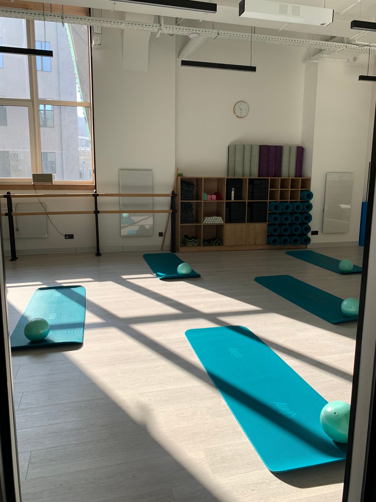 Sunlit Pilates studio prepared with mats, exercise balls and props